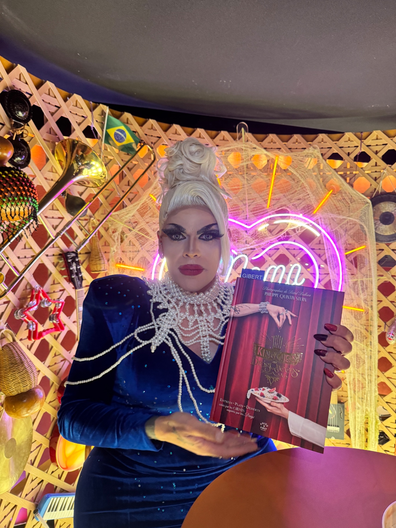 Artiste drag en robe bleue présentant un livre sur scène
